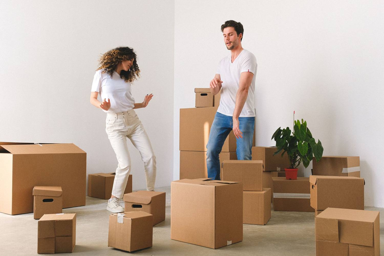 Couple heureux dansant parmi des cartons dans une pièce lumineuse, symbolisant un jour de déménagement joyeux.